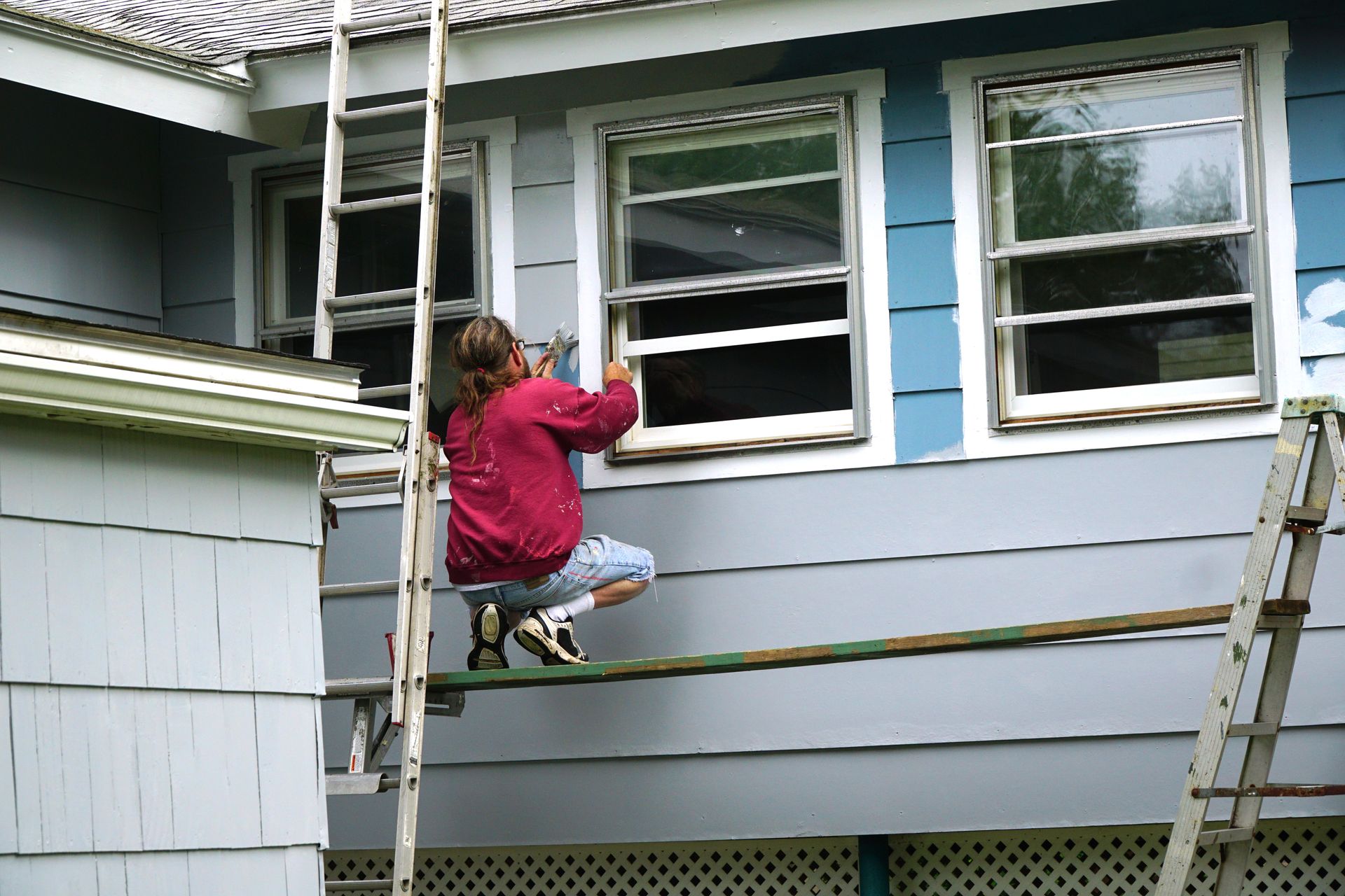 Person on scaffolding, cleaning windows of a blue house. Person on scaffolding, cleaning windows of a blue house.