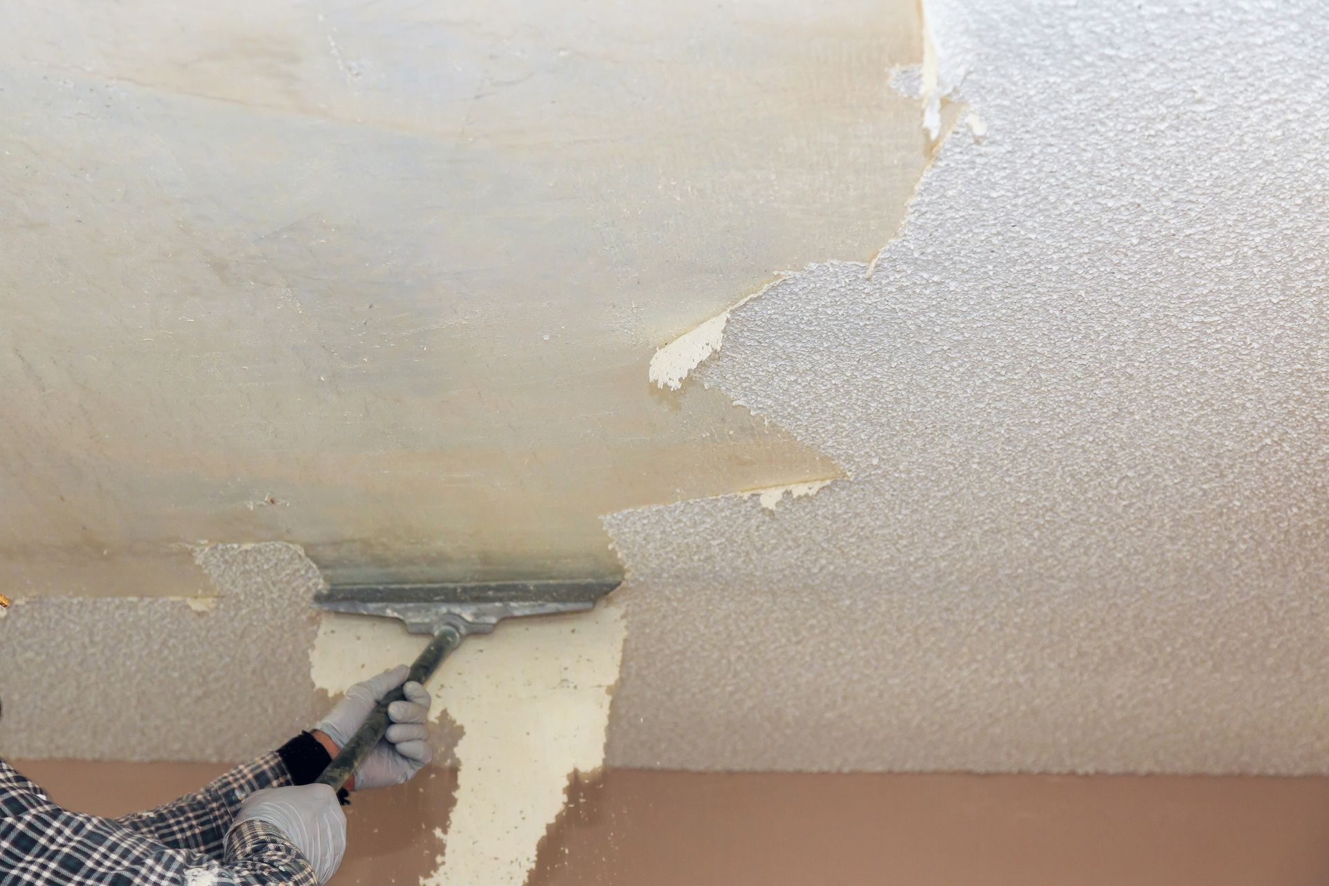 Person scraping textured ceiling with a metal tool, peeling off old material.