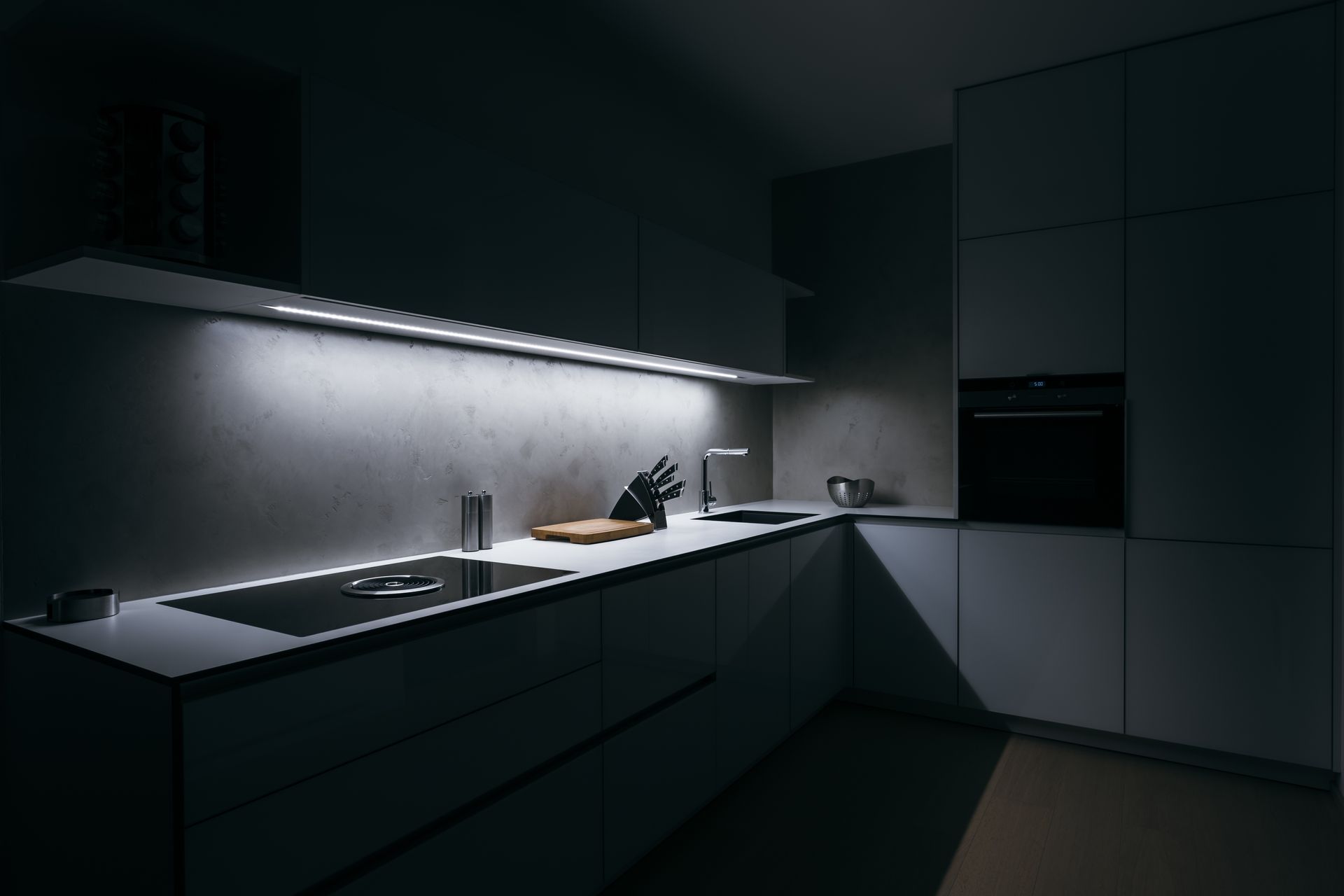Modern kitchen with under-cabinet lighting. Gray cabinets, stainless steel appliances, and a dark room lit by LED strips.