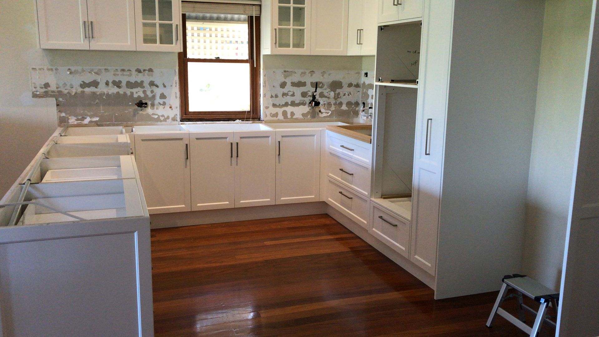 White kitchen cabinets with exposed backsplash, and dark hardwood floor.