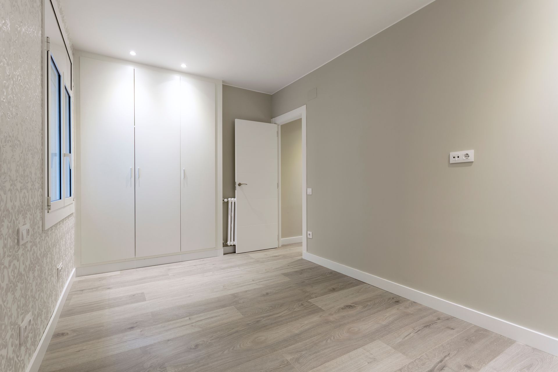 Empty, neutral-toned bedroom with built-in white closet, light wood-look flooring, and a closed white door.
