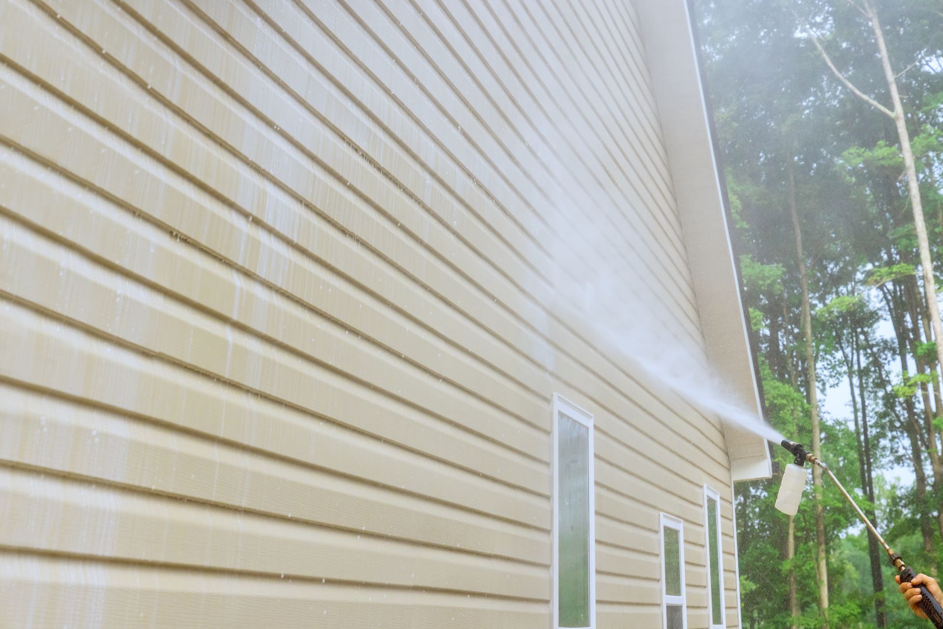 Power washer cleaning light beige siding on a house.
