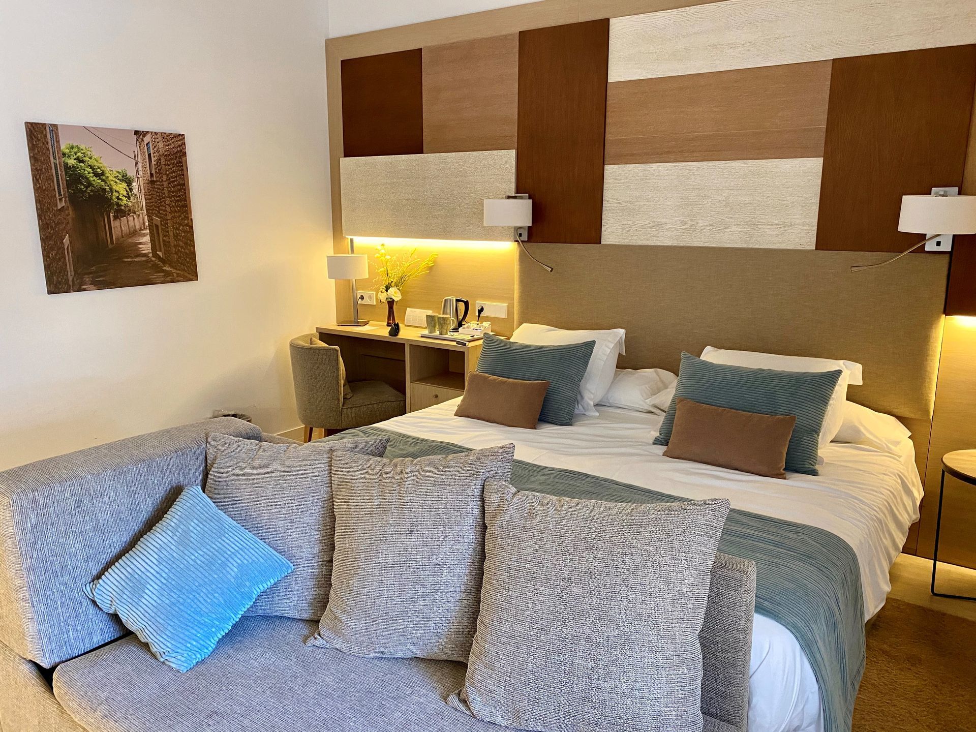 Chambre d'hôtel confortable avec un grand lit, des coussins décoratifs et un petit canapé près d'une fenêtre.