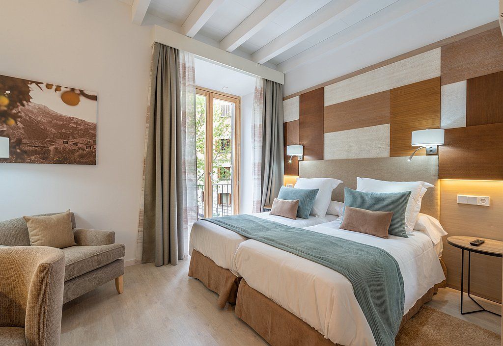 Chambre avec deux lits jumeaux, canapé et fenêtre. Tons beige et marron.