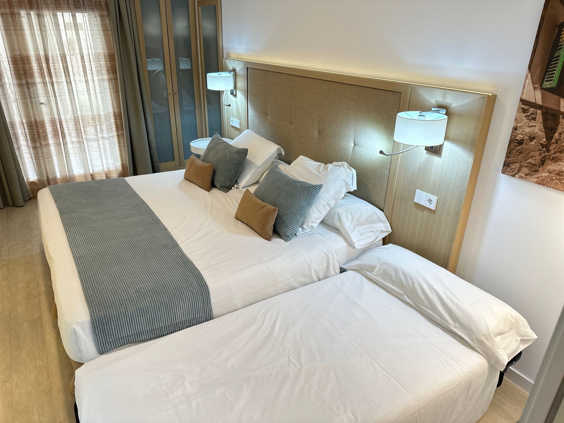 Habitación de hotel con camas para tres personas, sábanas blancas, almohadas azules y tostadas, cabecero de madera.