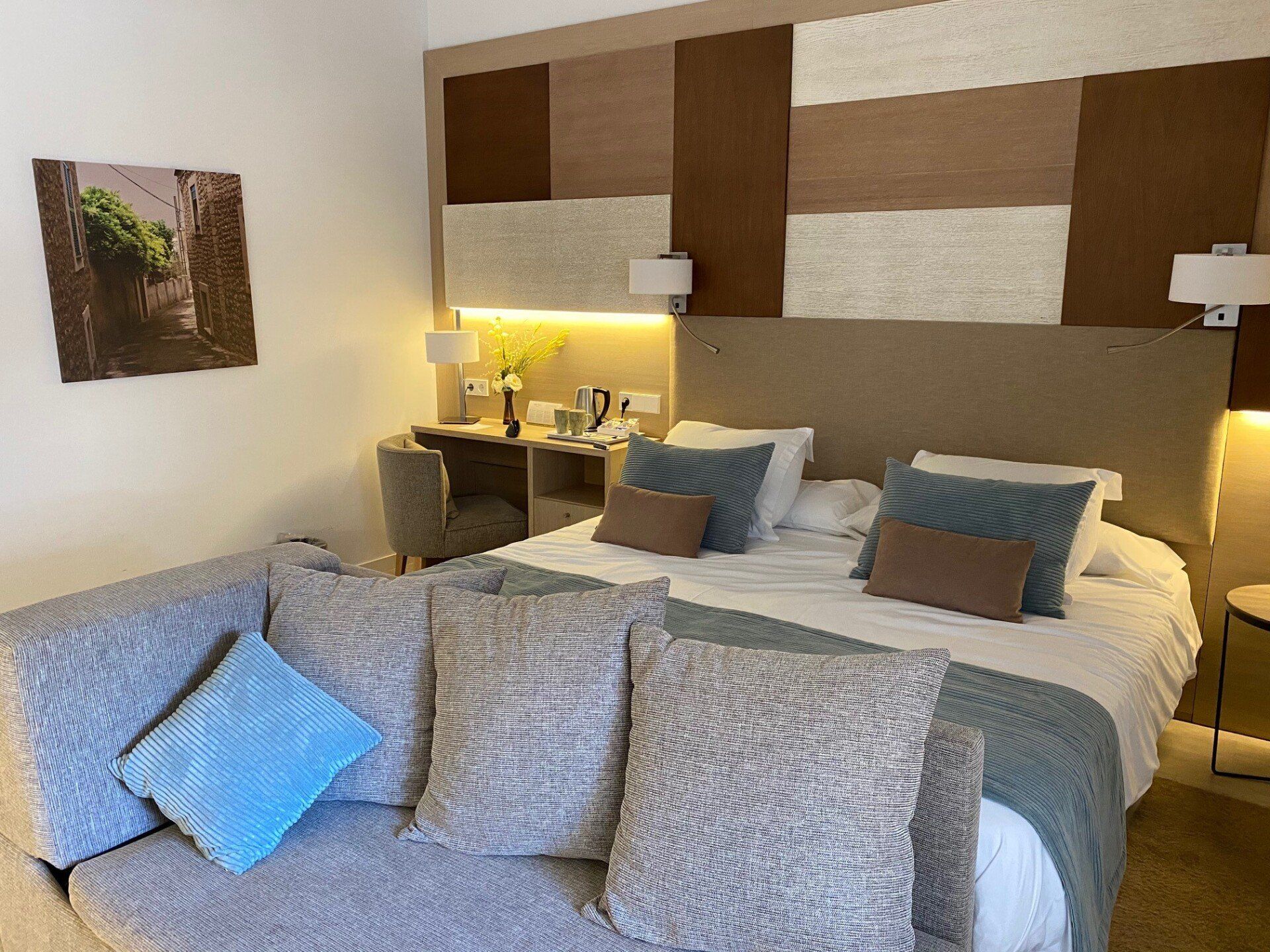 Chambre d'hôtel avec lit, canapé, bureau et décoration murale. Tons marron et neutres.