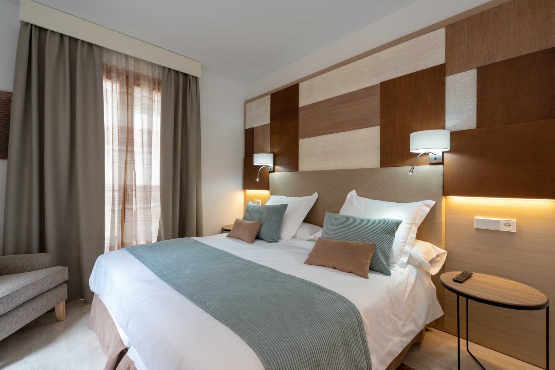 Chambre d'hôtel avec lit king size, tons neutres, tête de lit à motifs, fenêtre et table d'appoint.