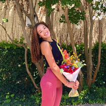 Picture of young black woman with long hair holding a bouquet of flowers in pink pants and a black tank top 
