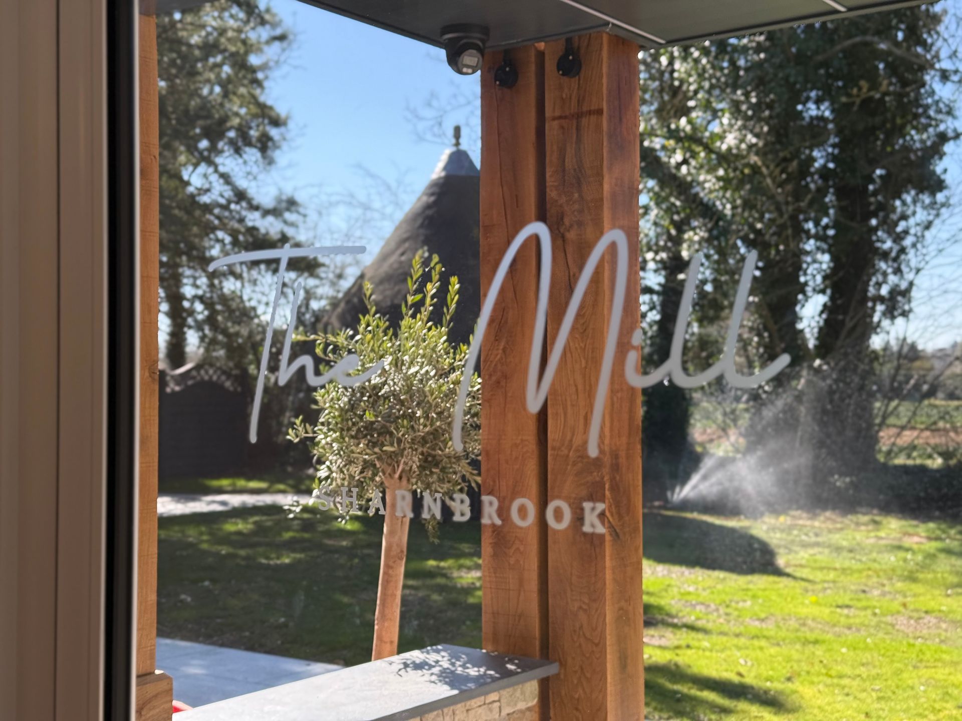 The Mill, Barnbrook signage on a window, with a thatched-roof building visible in the background.