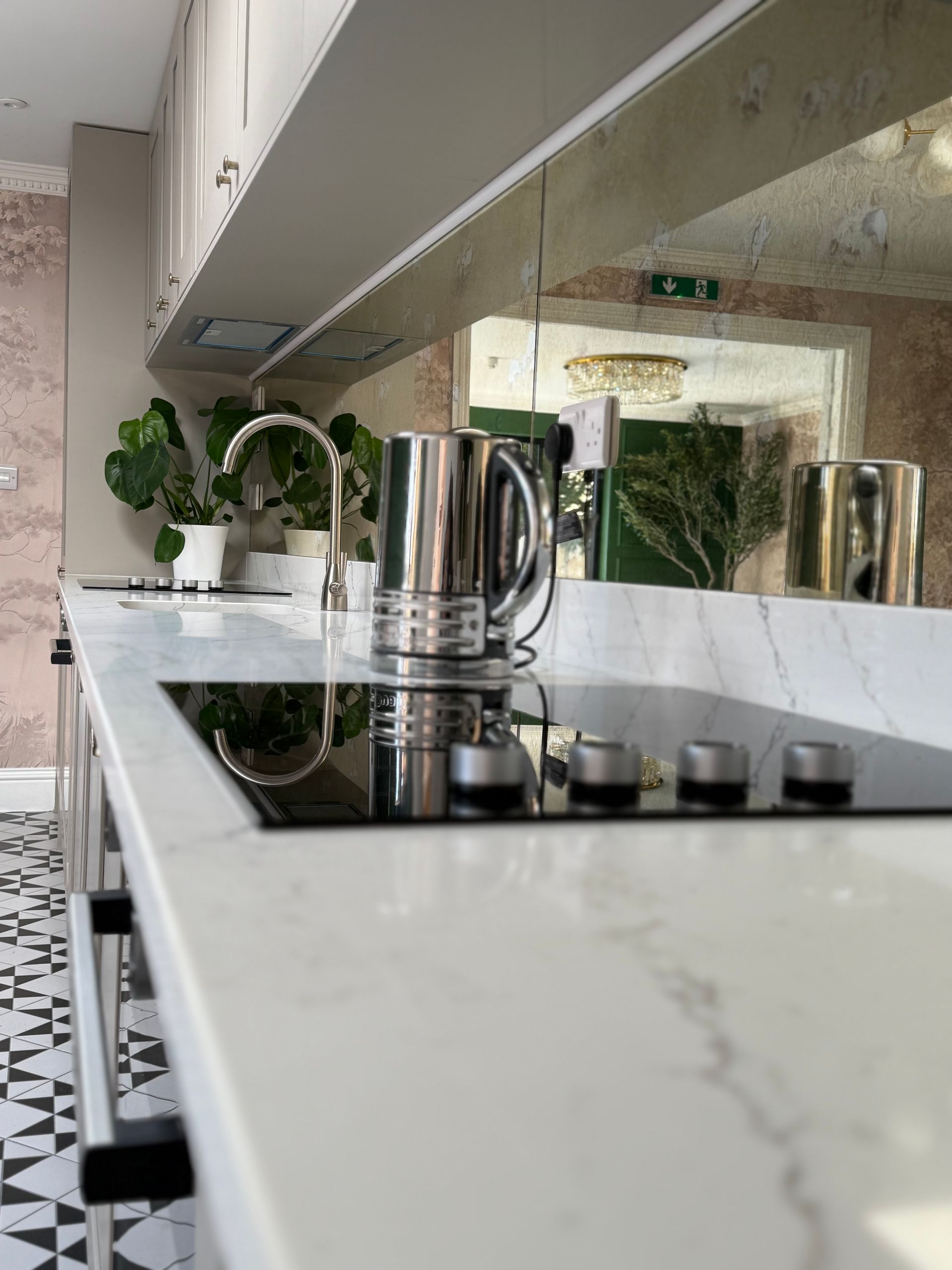 Modern kitchen with white countertop, stovetop, chrome faucet, and stainless steel kettle.