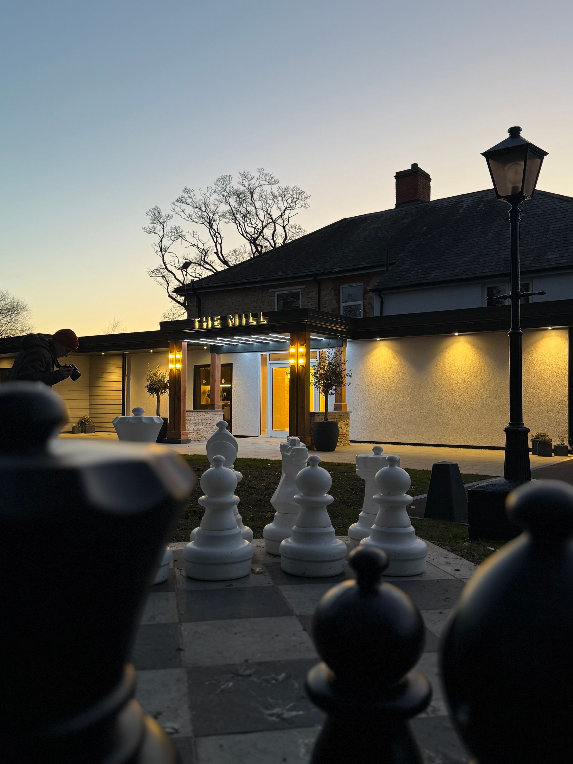 Giant chess set in front of a building with warm lighting at dusk.