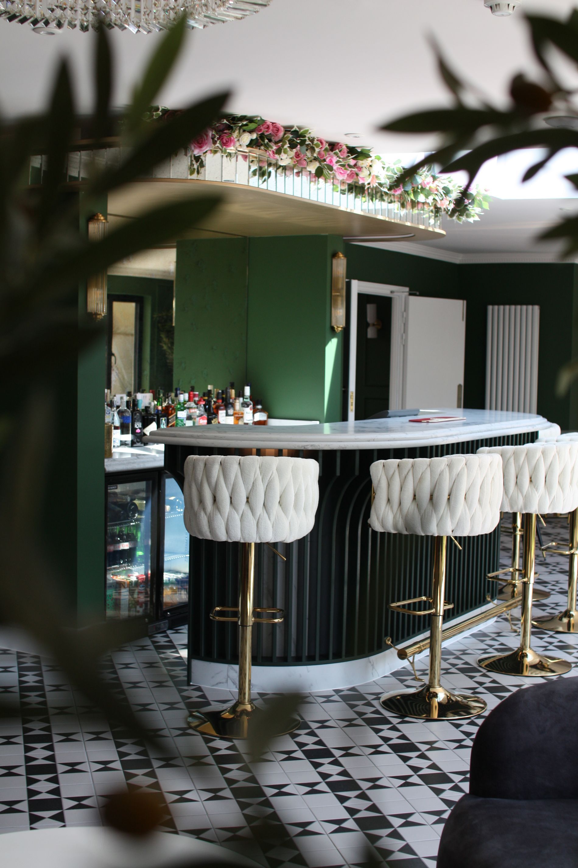 Bar with white marble countertop, fluted black front, gold stools, and olive green wall.