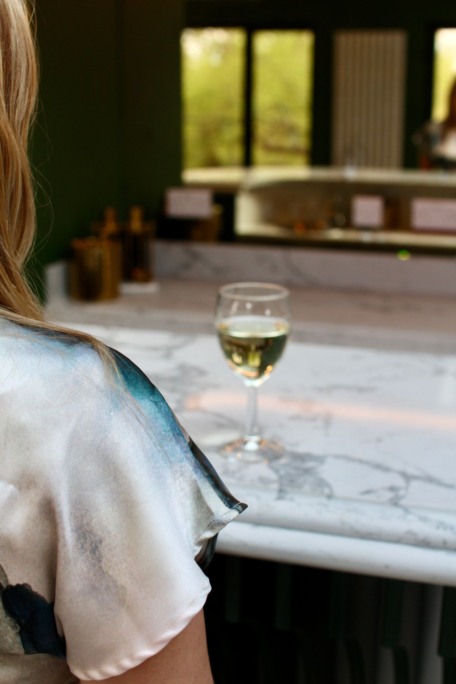 Woman at a bar with a glass of white wine on a marble countertop. Blurred background of a bar.