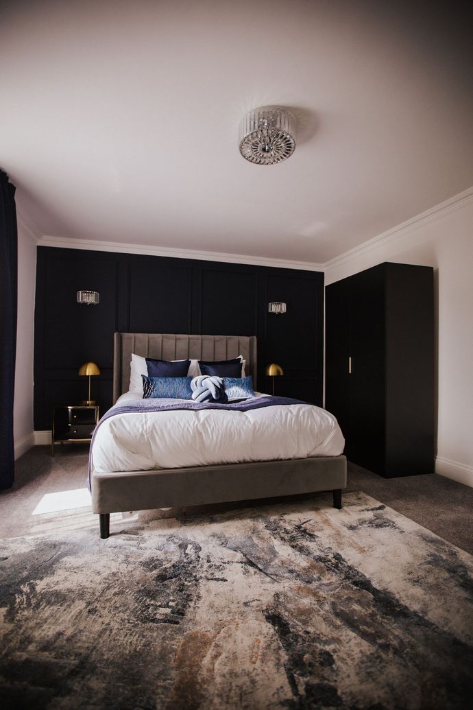 Bedroom interior with dark panel wall, bed, dresser, curtains, and gold chandelier.