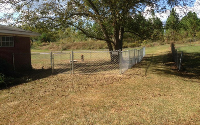 chain link fence with tree and side of brick house in the background