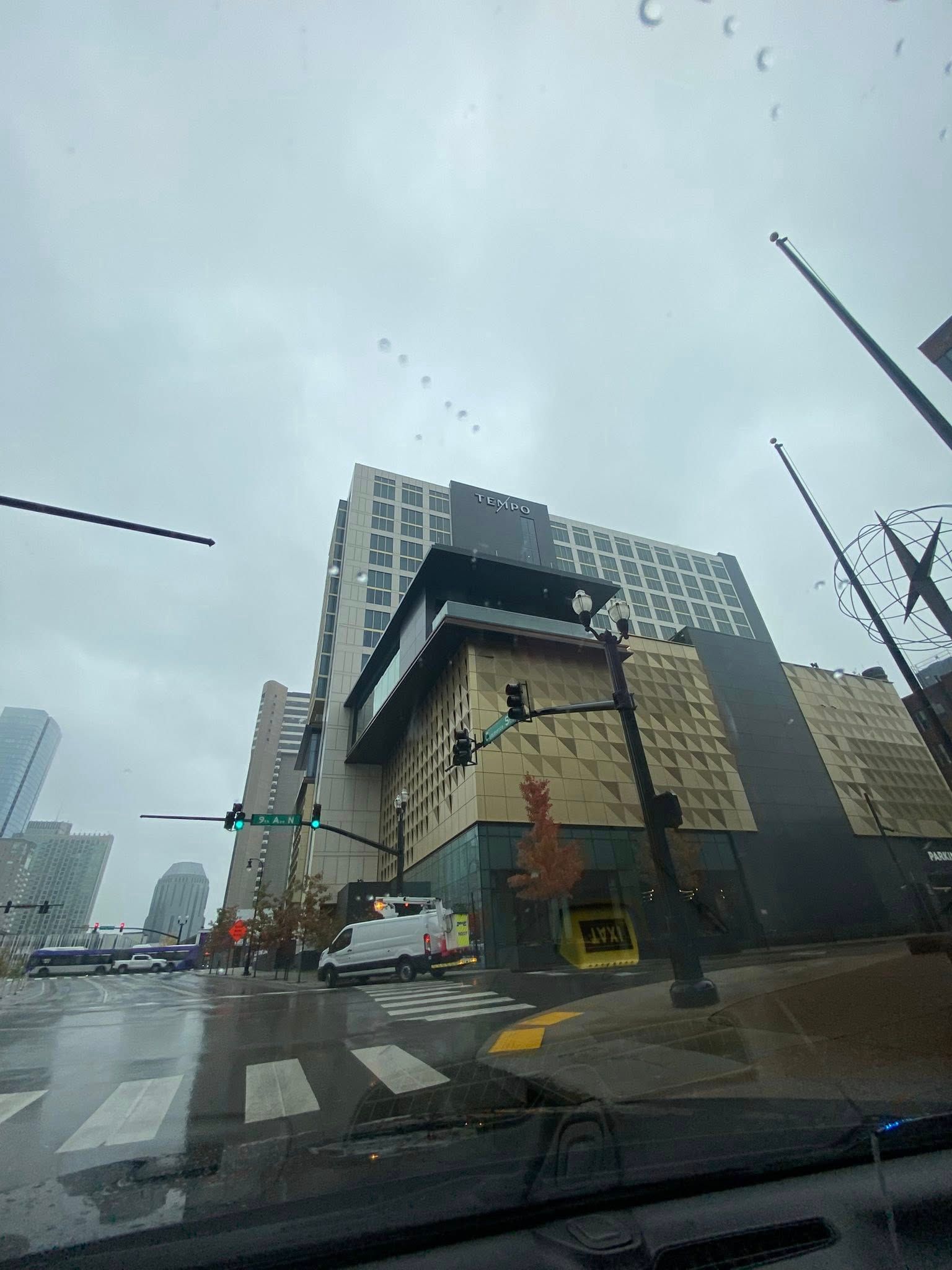 Man in car petting a golden retriever; city street in background.