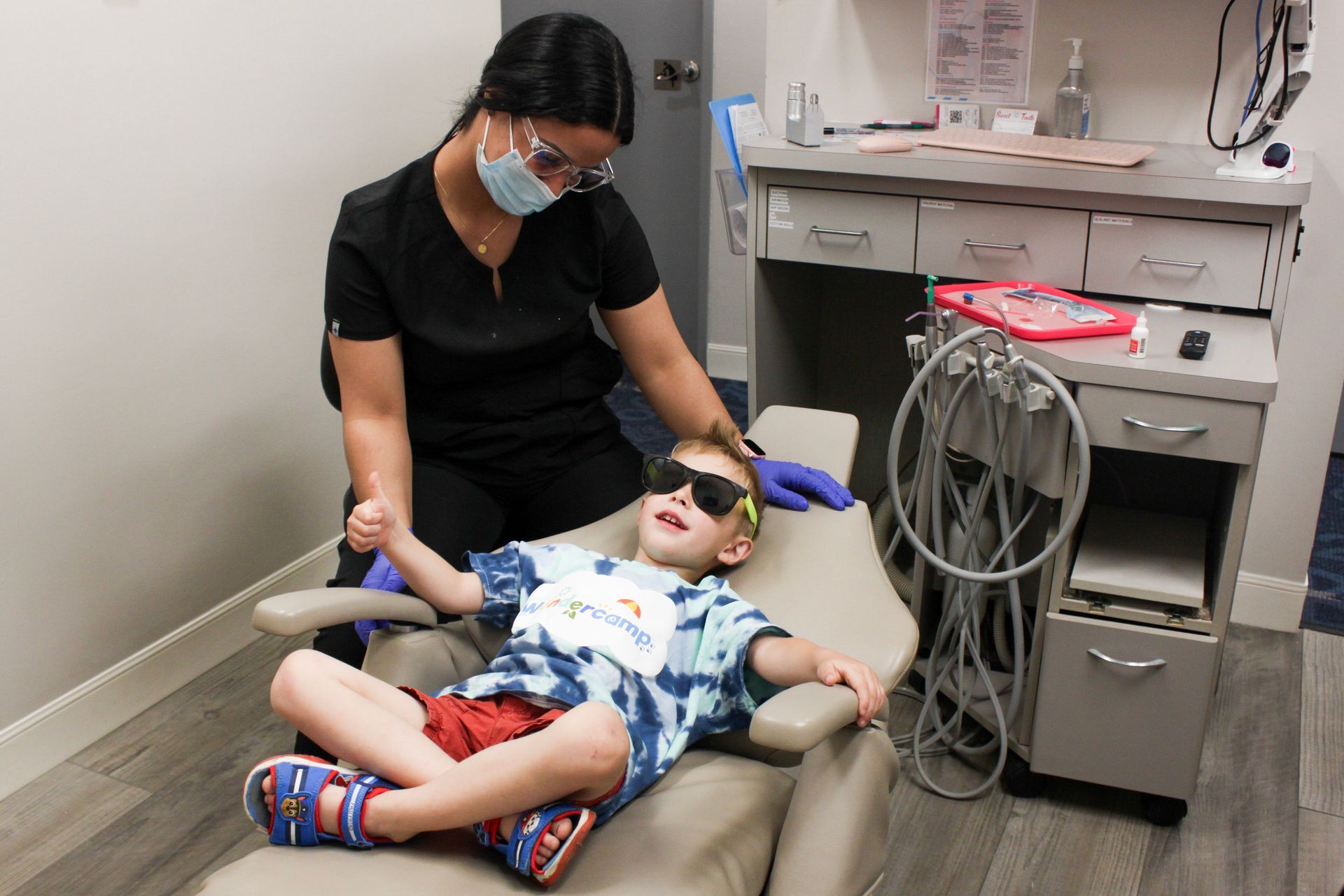 Little boy sitting in the patient chair next to a dental assistant. 