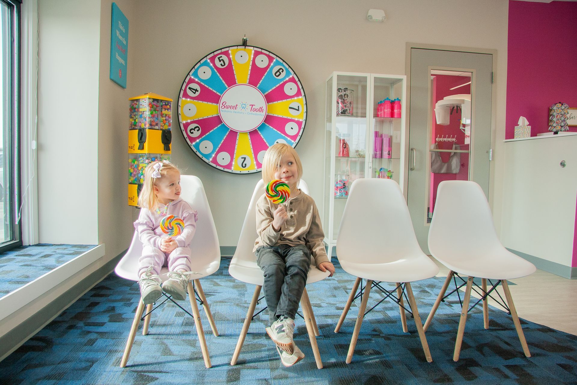 A little boy and girl sitting on lobby chair at a dentist holding lollipops. 