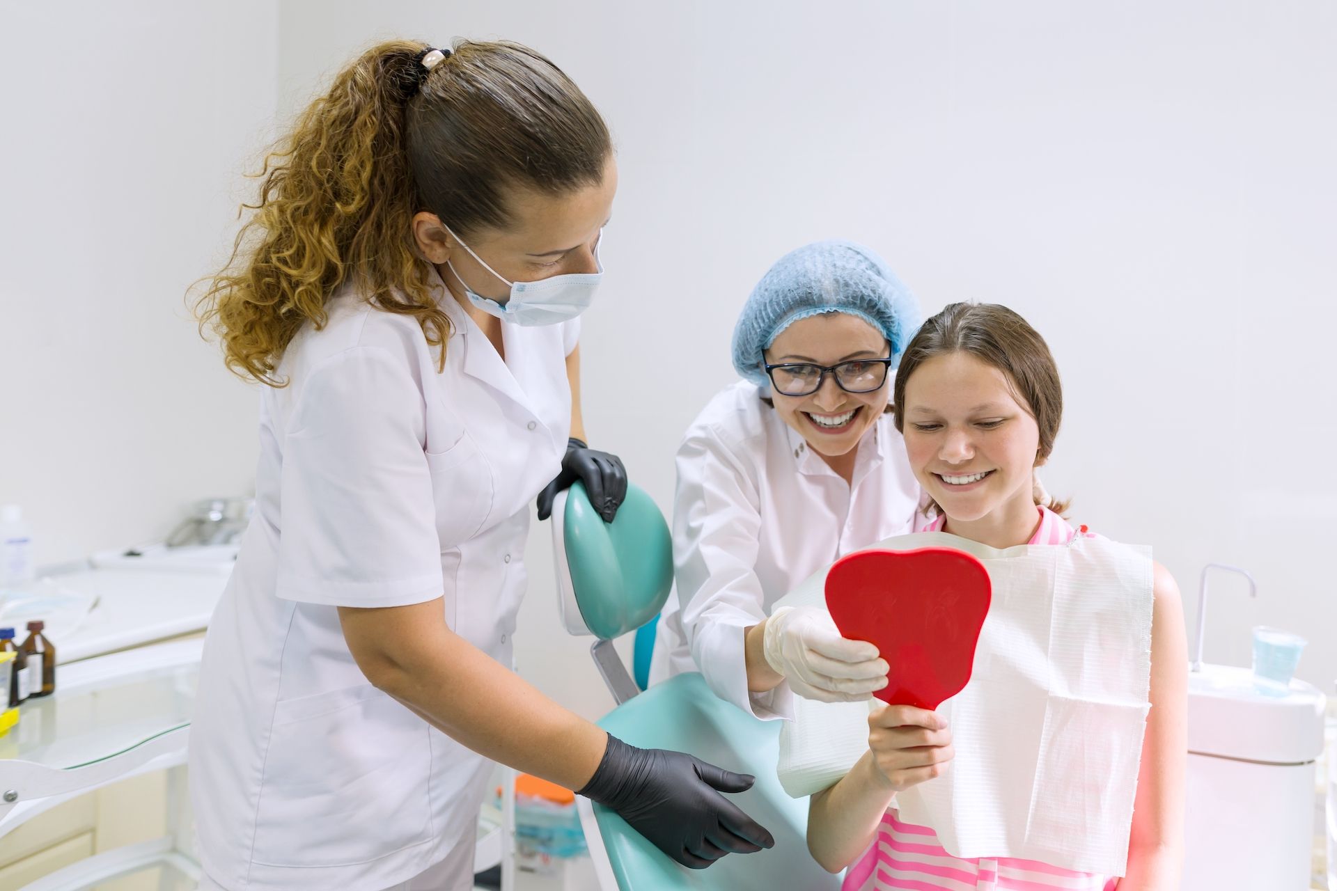 A girl is sitting in a dental chair looking at her teeth in a mirror.