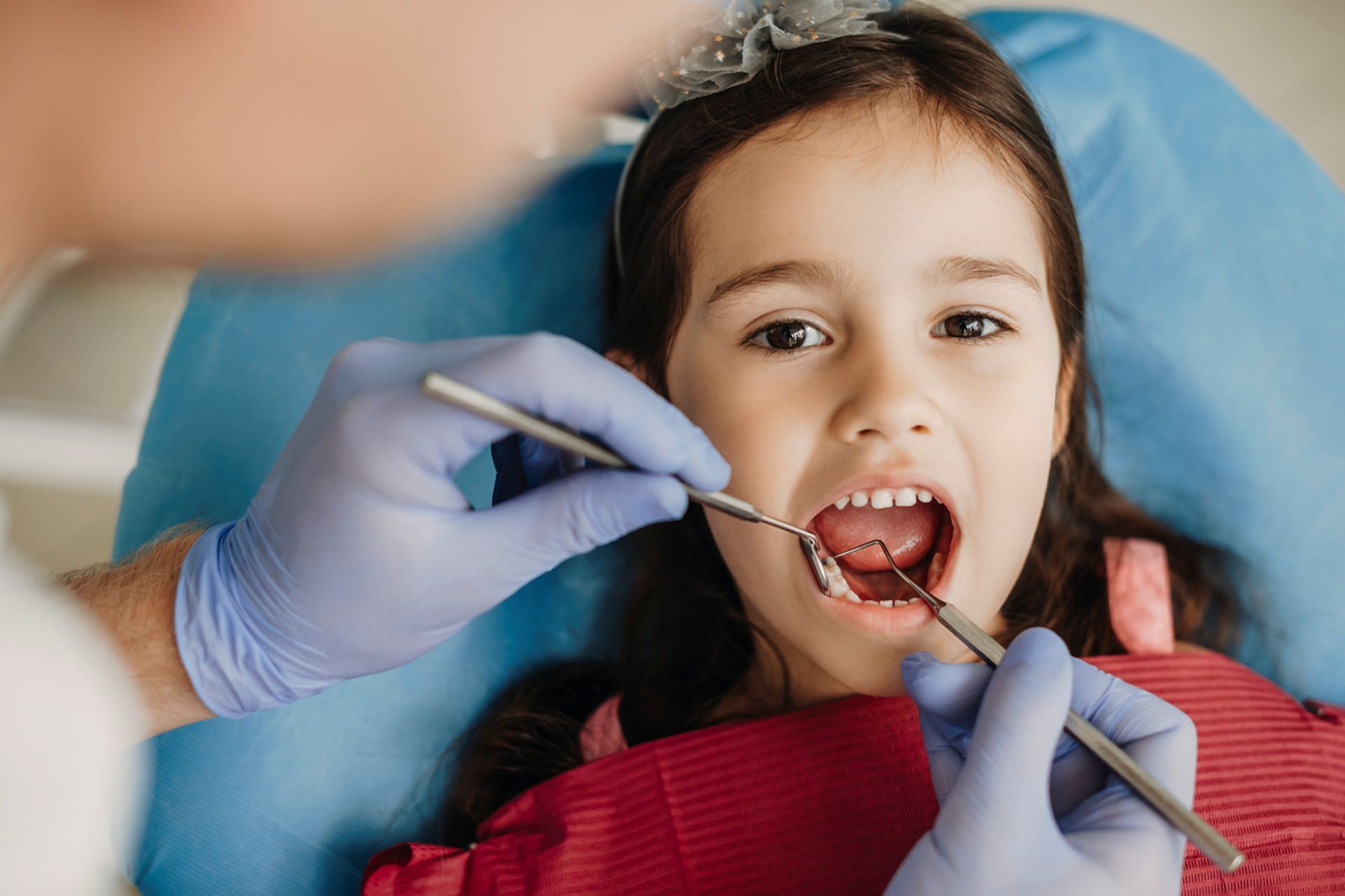 Young girl looking at camera during dentist appointment, dentist's hands with blue gloves
