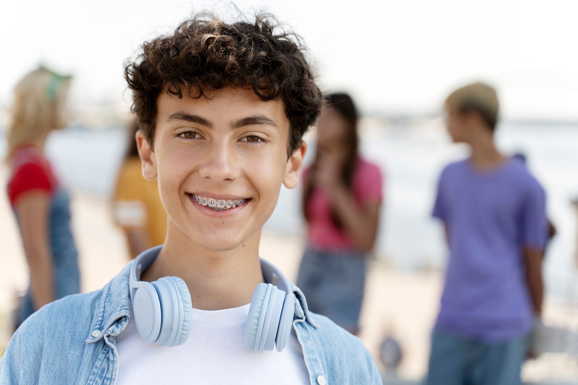 A young boy with braces and headphones is smiling in front of a group of people.