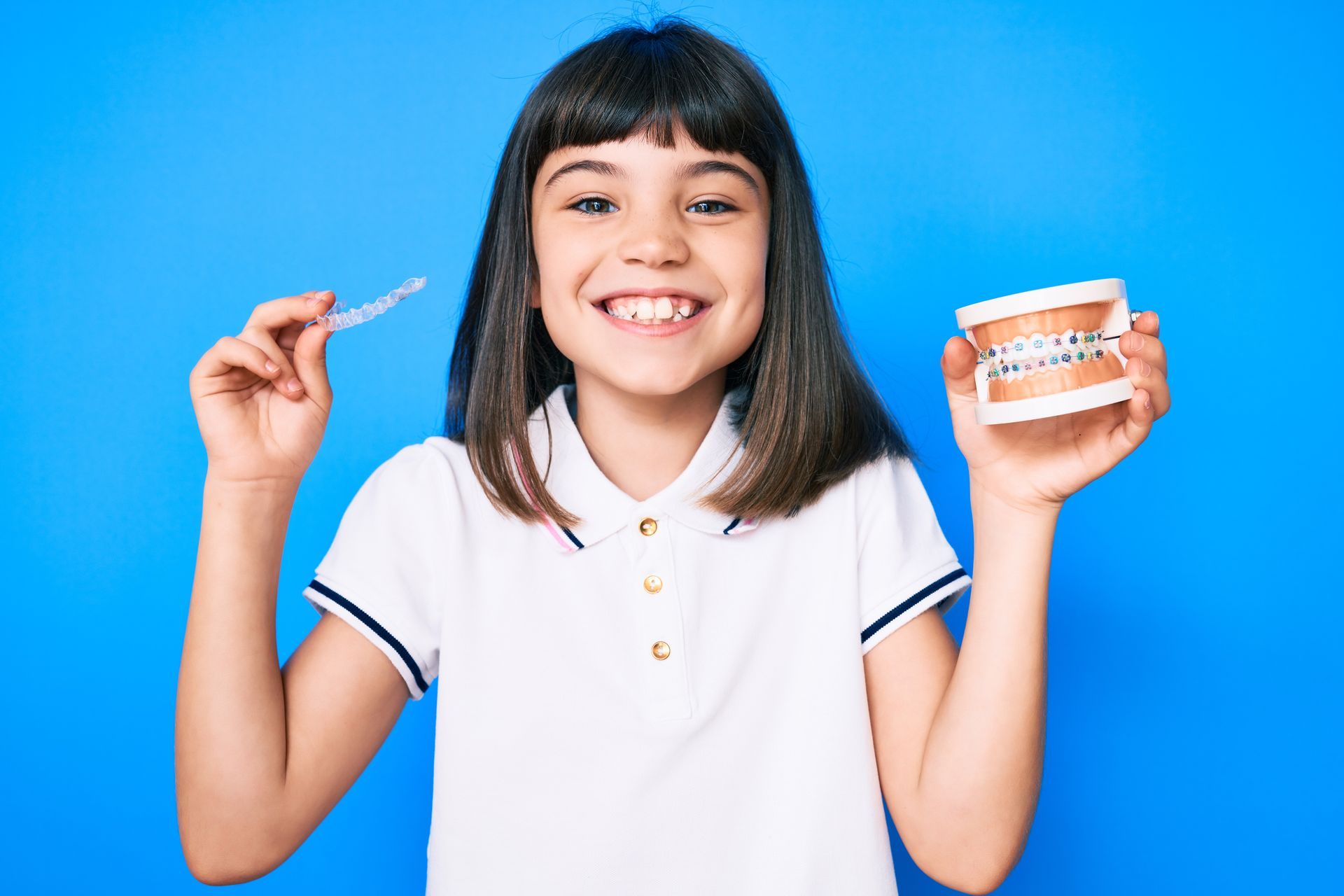 A young girl is smiling and holding a retainer  and braces.