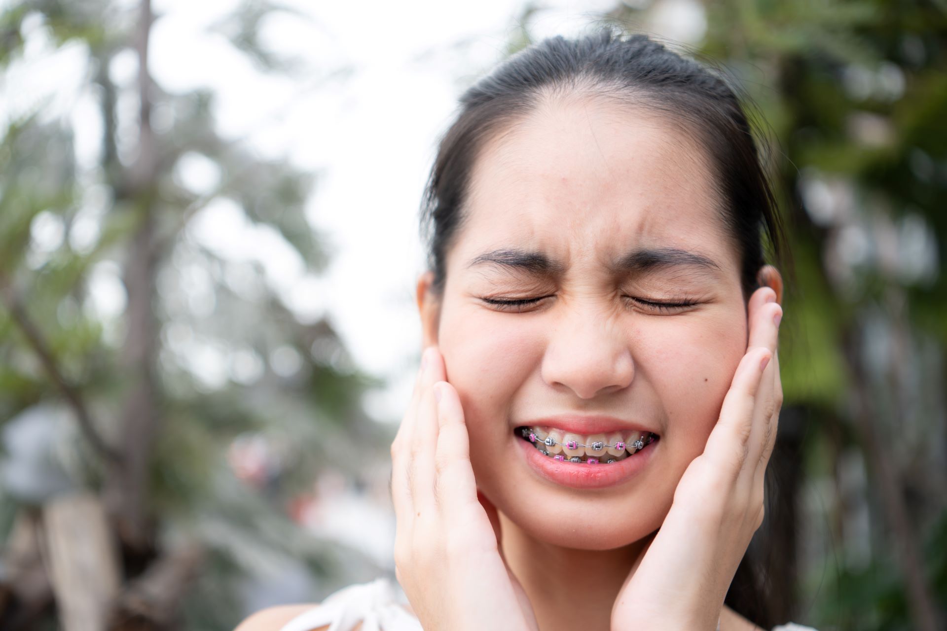 A woman with braces on her teeth is holding her face in pain.