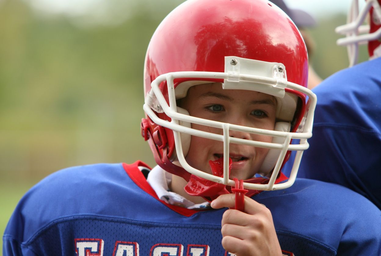 Young boy putting on a sports mouth guard during a football game.