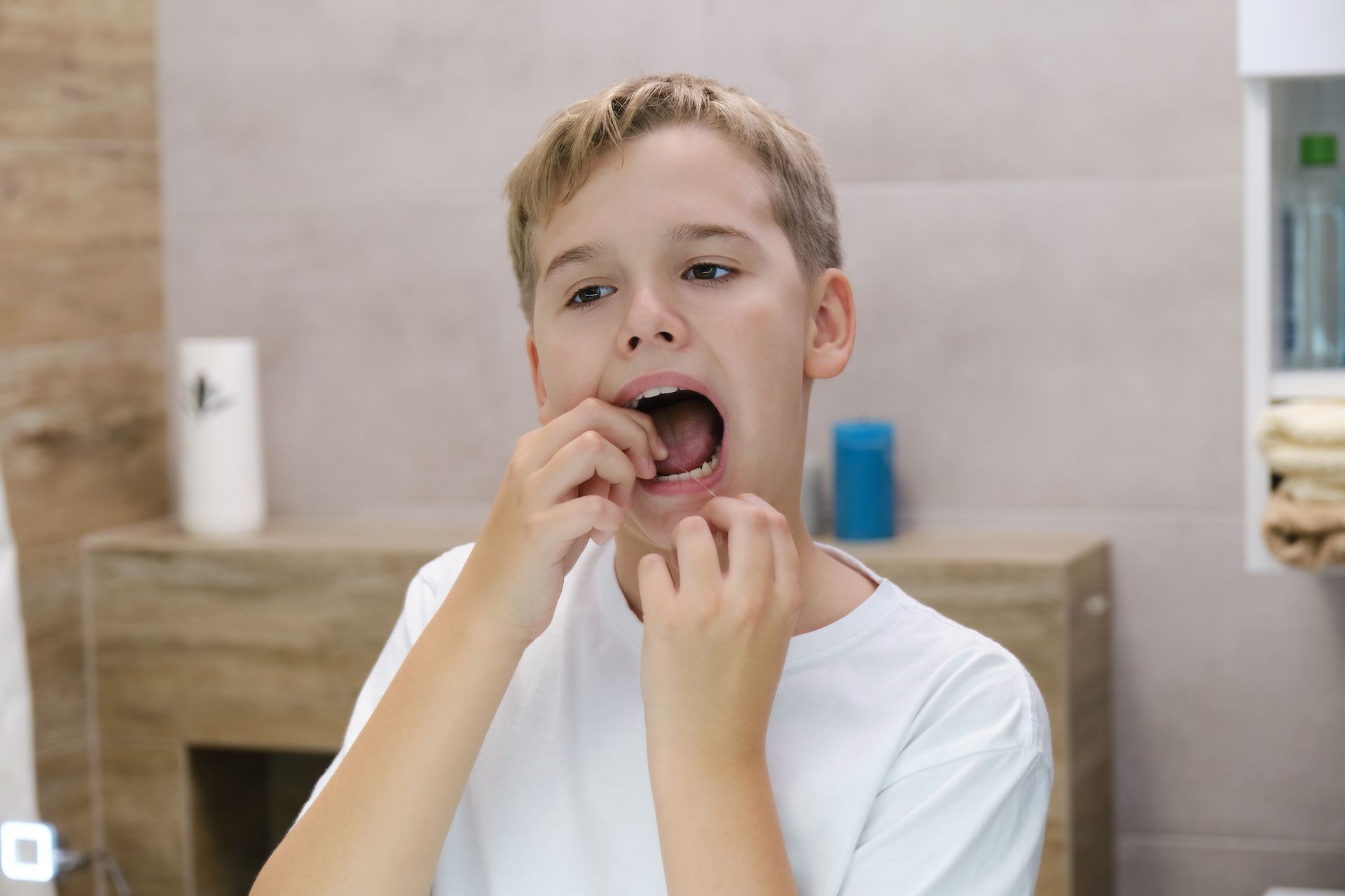 A young boy is flossing his teeth in front of a mirror.