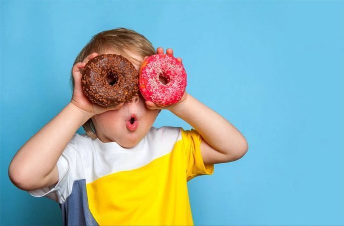 A young boy is holding two donuts in front of his eyes.