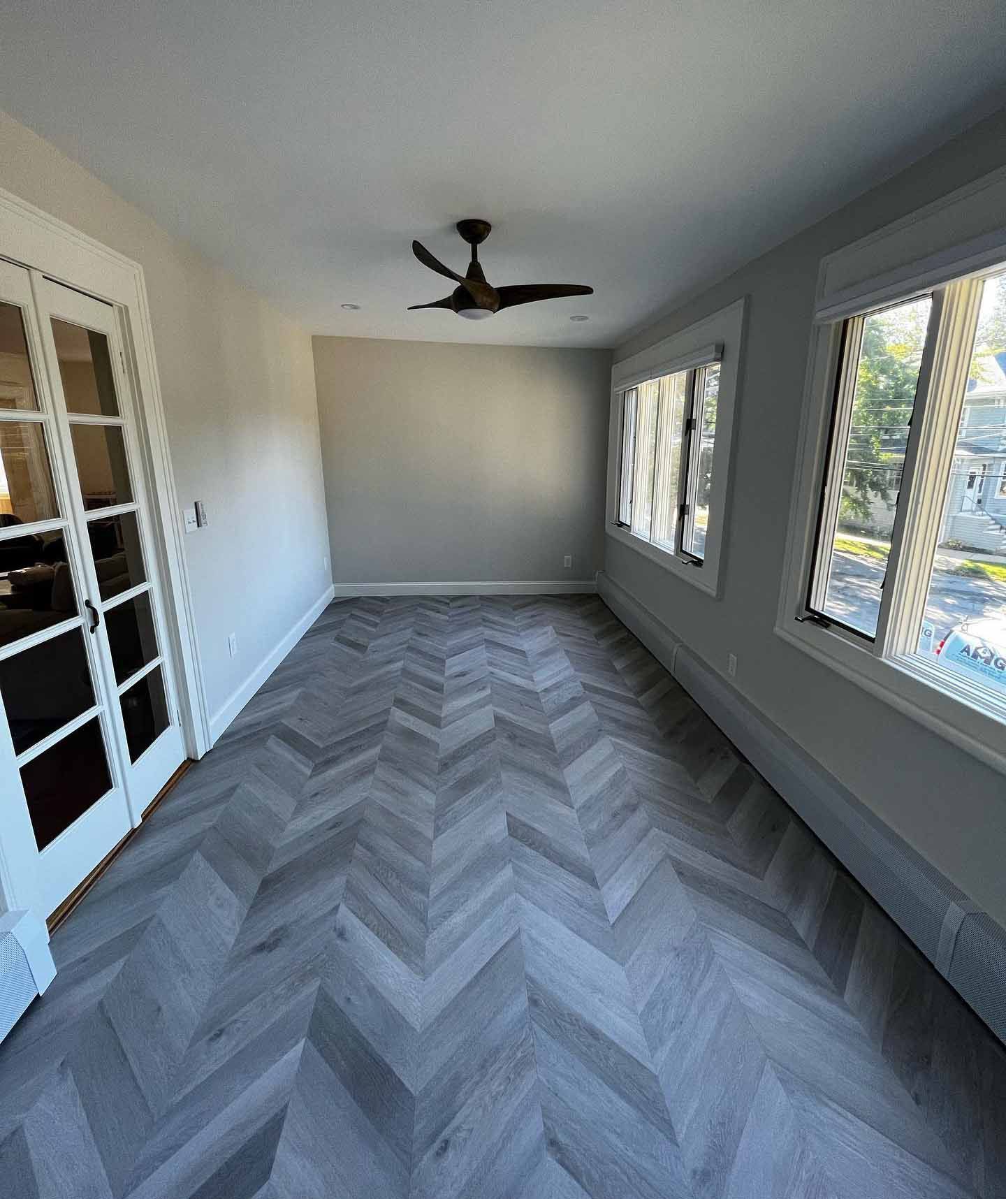 A living room with a herringbone floor and a ceiling fan.