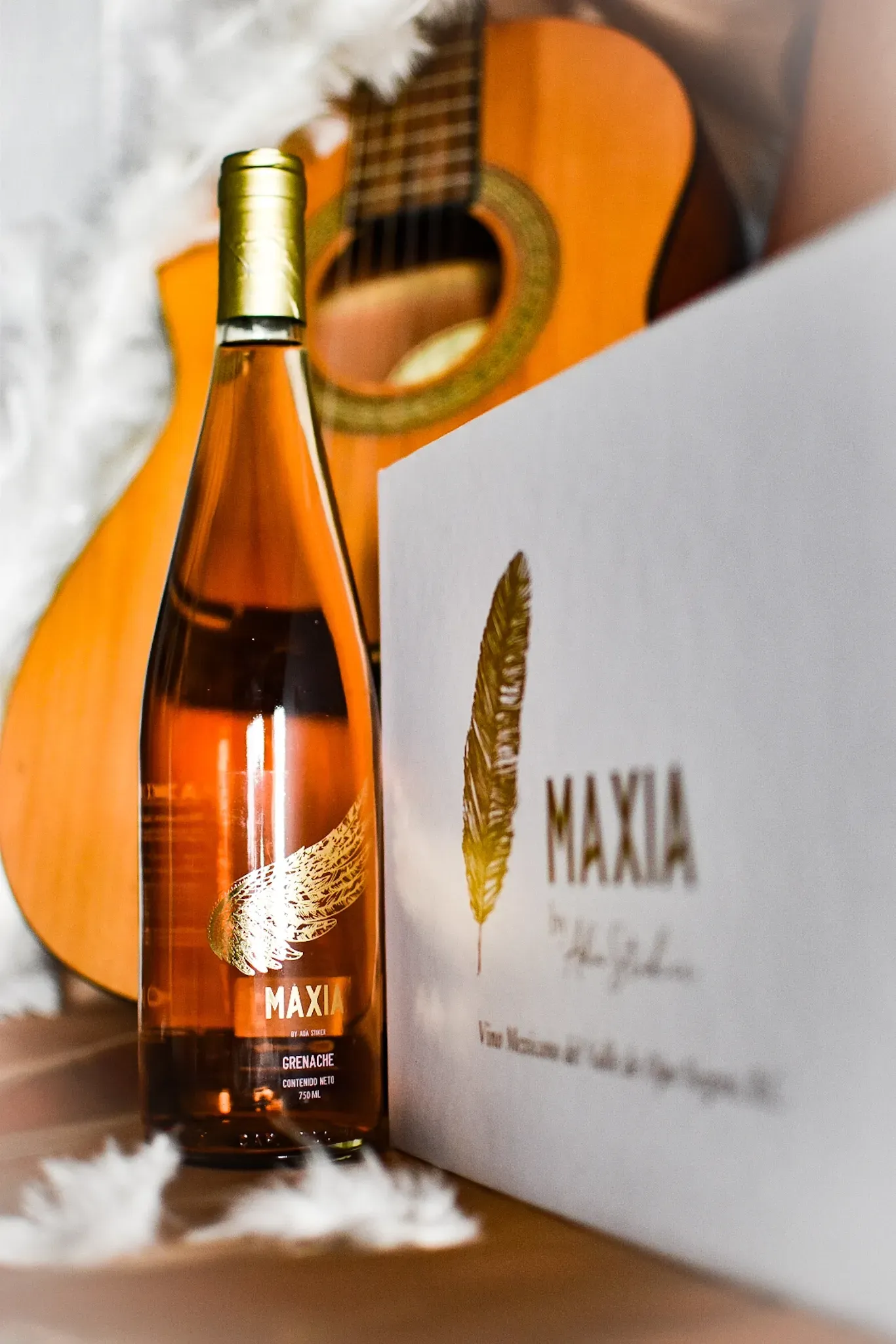 Botella de vino MAXIA, caja y guitarra acústica en un entorno suave y luminoso.