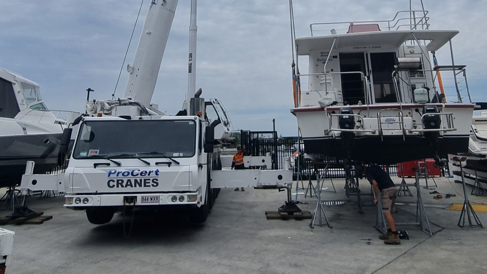 A White Crane Lifts a Boat at a Harbor, a Person is Working Under It — ProCert Cranes In Coolum Beach, QLD