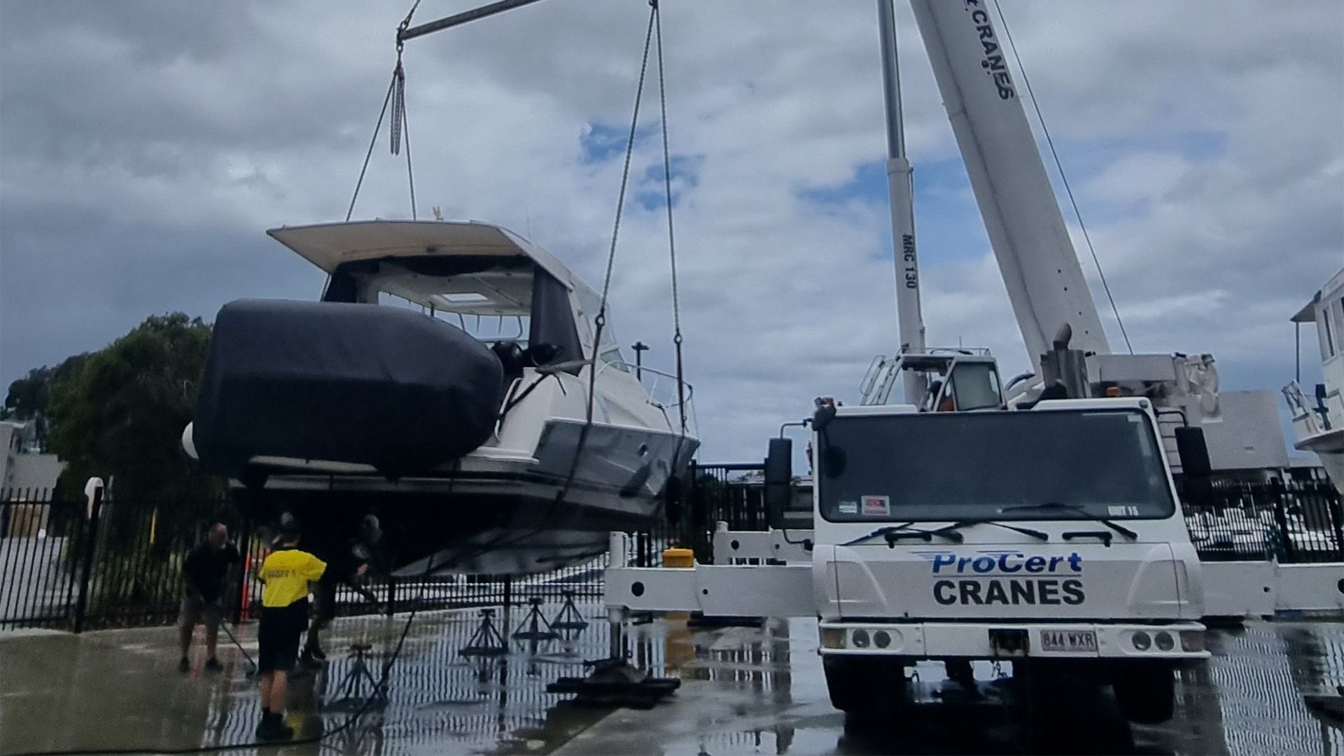 A Crane Lifts a Boat at a Dock. Workers in Yellow Vests Supervise — ProCert Cranes In Coolum Beach, QLD