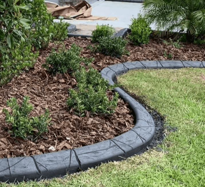 A lawn with a concrete curb and a garden in the background.