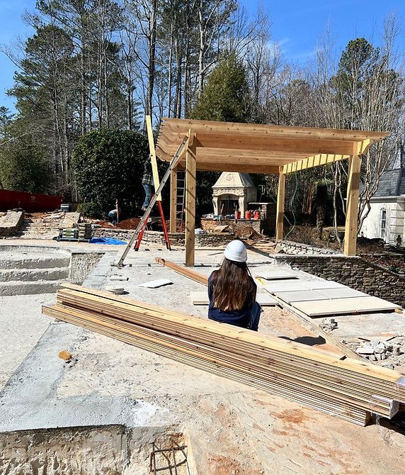 A woman is sitting on the ground in front of a wooden structure under construction.