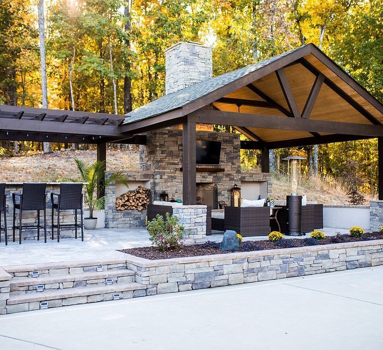 A patio with a pavilion and a fireplace in the woods.
