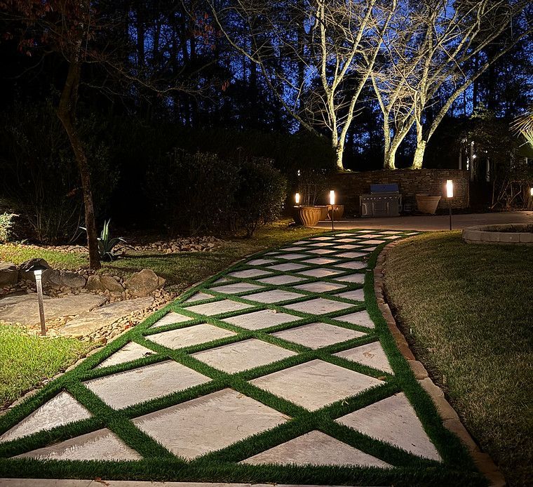 A walkway with grass on it is lit up at night.