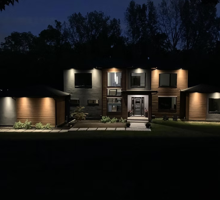 A large house is lit up at night with trees in the background