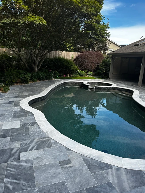 A large swimming pool is surrounded by a tiled patio and trees.