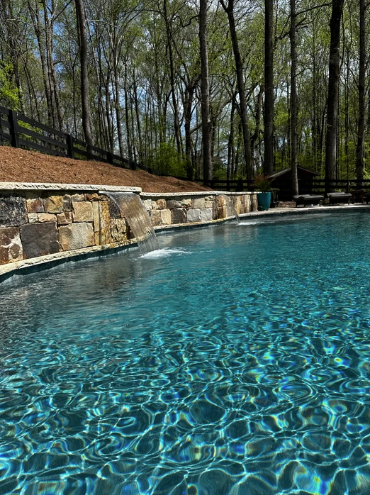 A large swimming pool surrounded by trees and a stone wall.