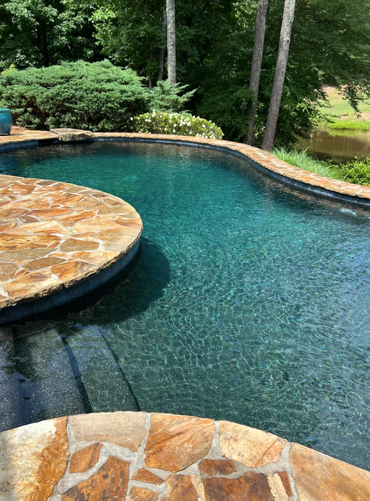 A large swimming pool with a stone deck and trees in the background.