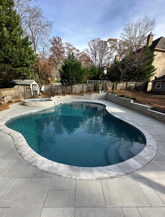A large swimming pool surrounded by trees and a fence in a backyard.