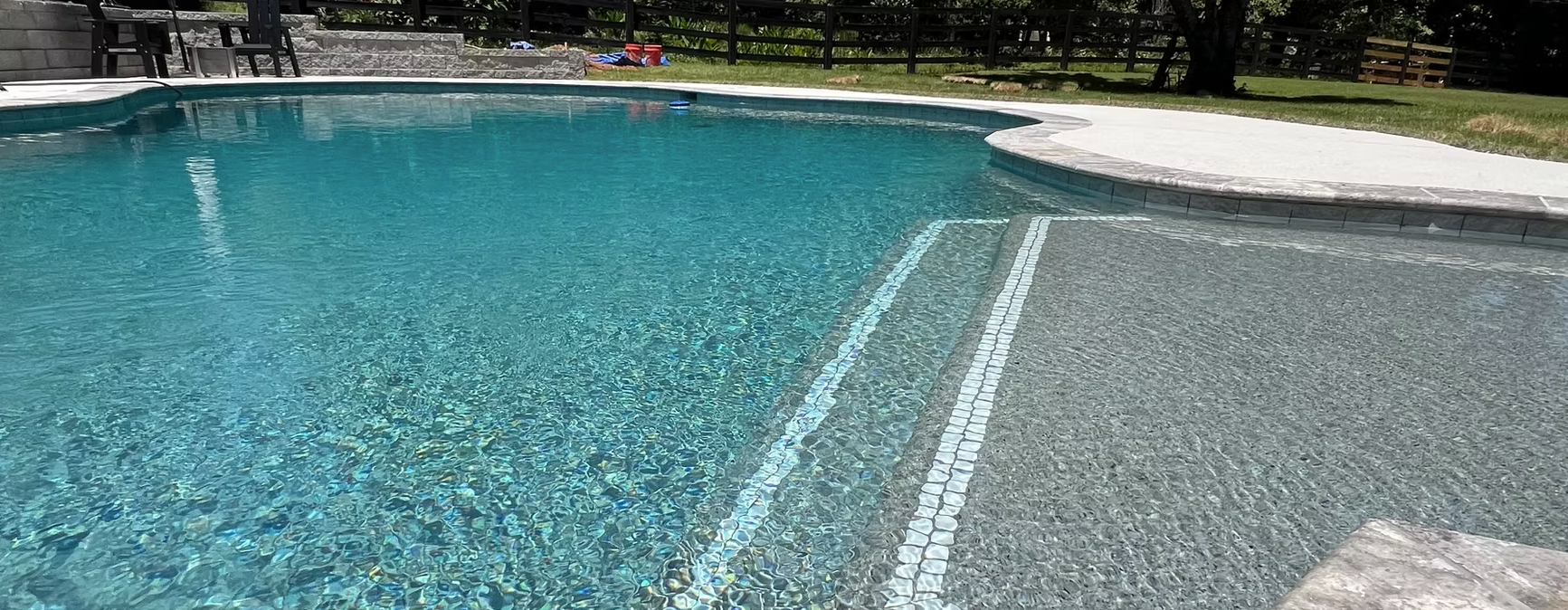 A large swimming pool with stairs leading to it in a backyard.