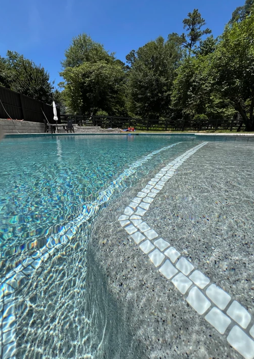 A swimming pool with a stone border and trees in the background