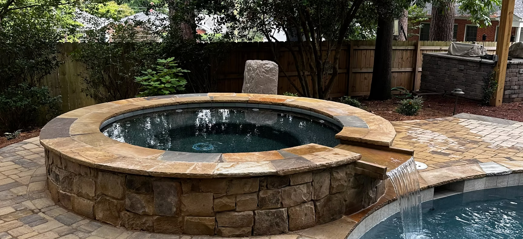 A hot tub is surrounded by a stone wall next to a pool.