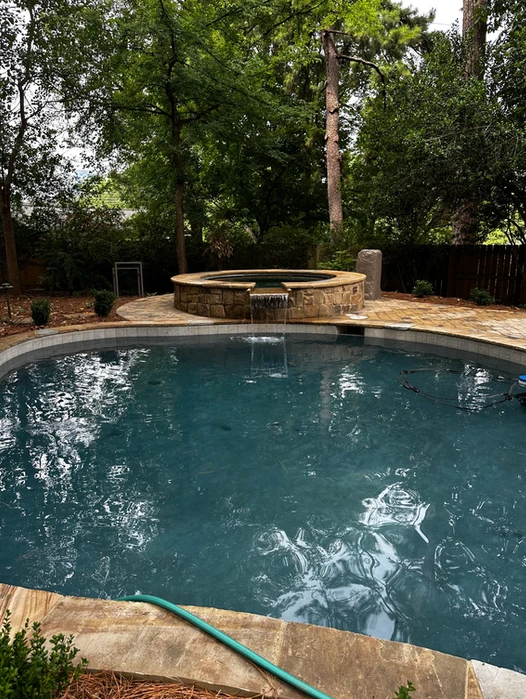A large swimming pool with a hot tub in the middle of it surrounded by trees.