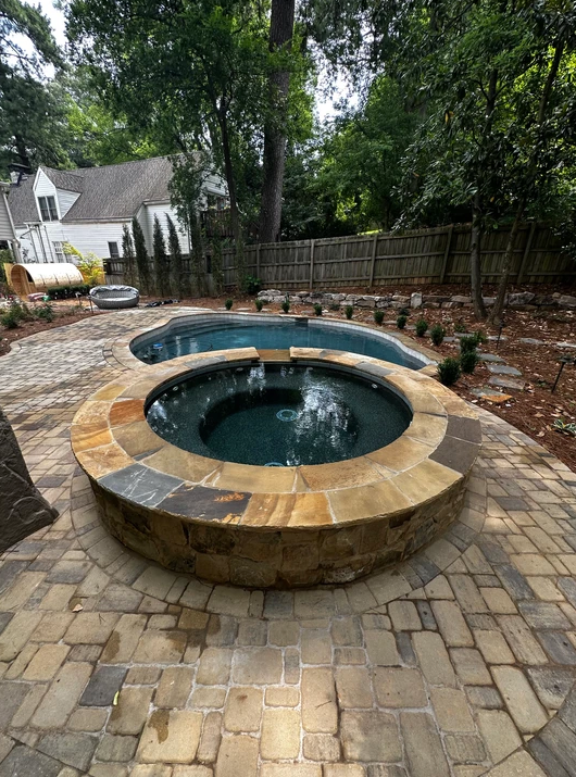 There is a hot tub in the middle of a patio next to a pool.