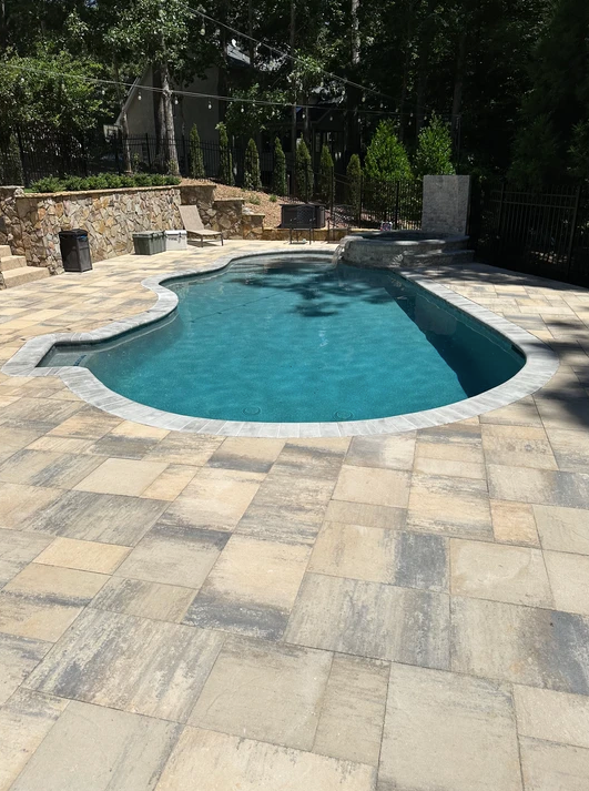 A large swimming pool is surrounded by a patio and trees