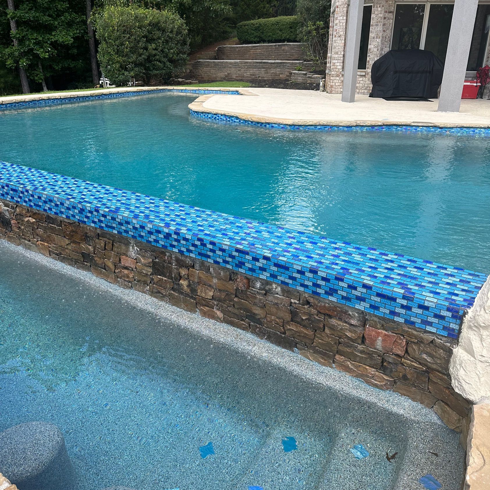 A large swimming pool with blue tiles and a stone wall surrounding it.